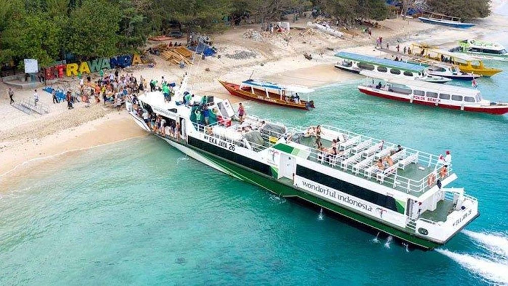 A ferry with passengers, a beach, and other boats in the background. 1