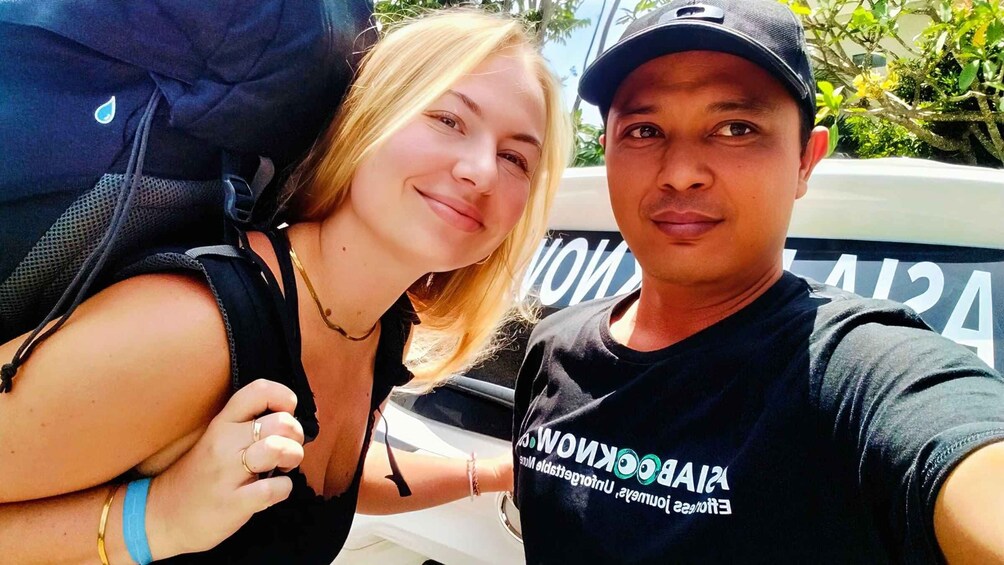 Dos personas tomándose un selfie con un vehículo al fondo. 1