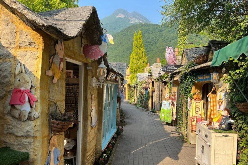 A narrow street lined with stone buildings, some with colorful decorations and signs, leading towards a mountain in the background. 2