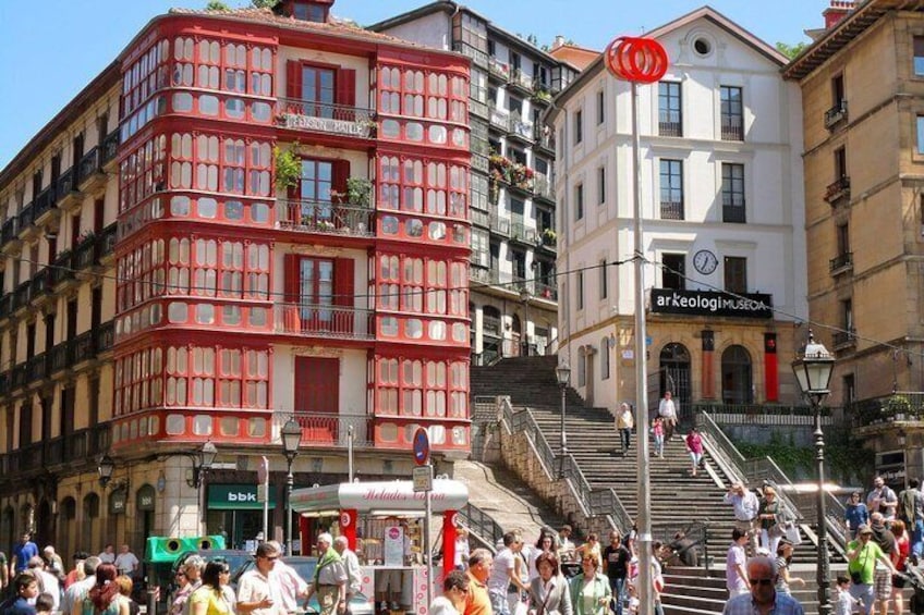 A busy street with a red building, a white building with a clock, and a sign for 'ArkeologiMUSEO.' 3
