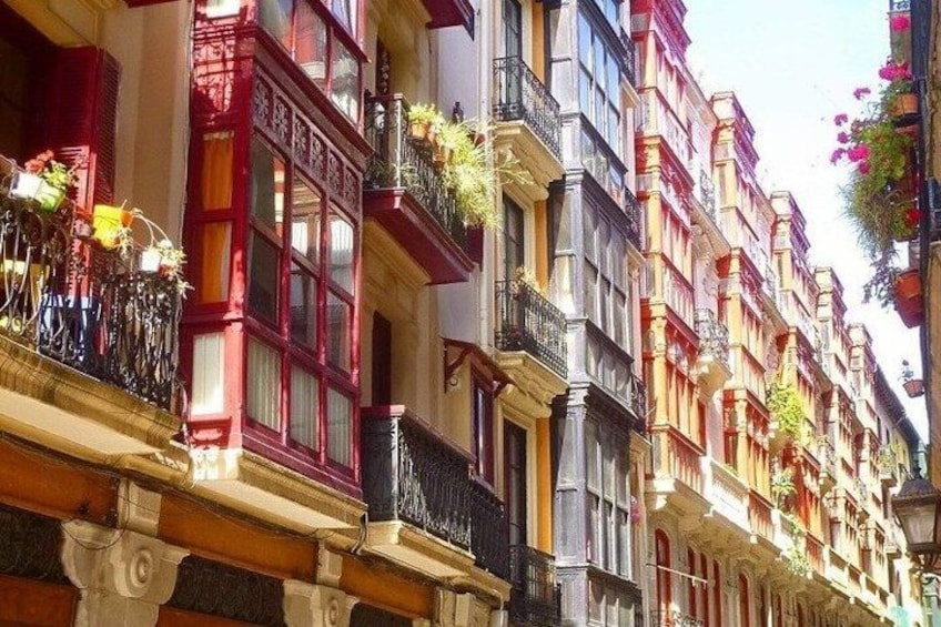 A row of colorful buildings with balconies adorned with plants. 1