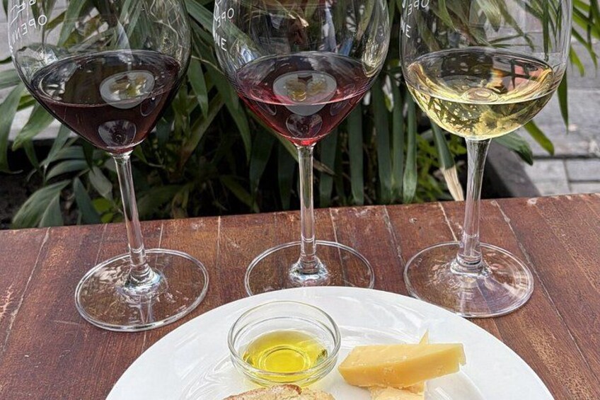 Tre bicchieri da vino su un tavolo di legno, con un piatto di formaggio e una piccola ciotola di olio d'oliva. 2