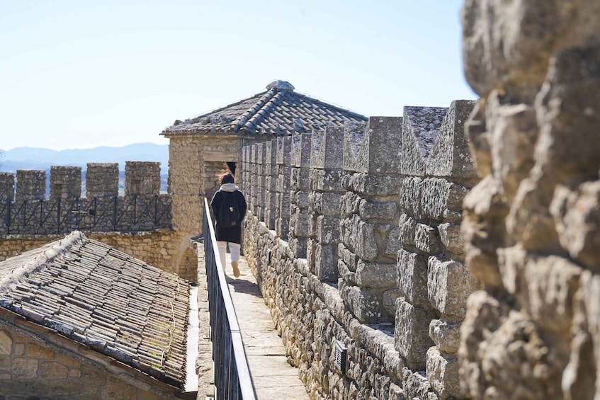 A stone wall with a tiled roof and a person walking along a pathway. 1