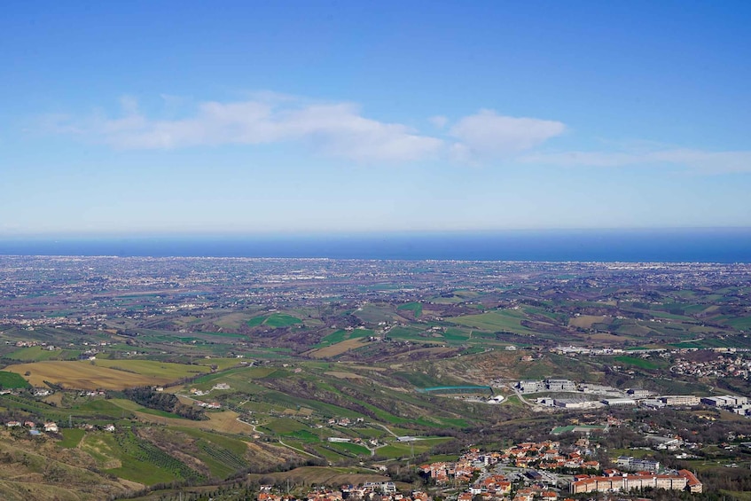 A panoramic view of a coastal town with rolling hills, a river, and a distant city skyline. 2