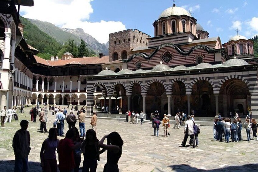 A historic courtyard with arches, a large building with domes, and mountains in the background. 3