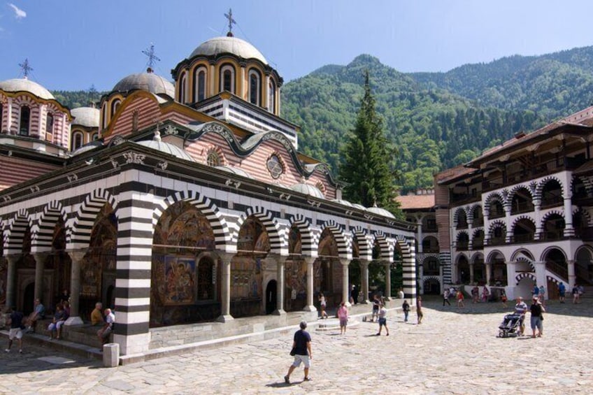 A historic building with arches and domes, surrounded by a cobblestone courtyard and lush green mountains. 1