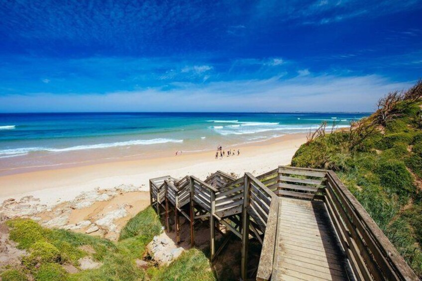 A beach with wooden walkways leading to the shore, clear blue sky, and calm ocean waves. 4