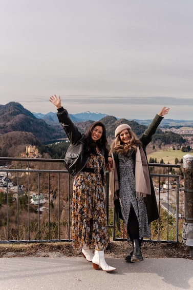 Two people standing on a balcony with a mountainous landscape in the background. 5