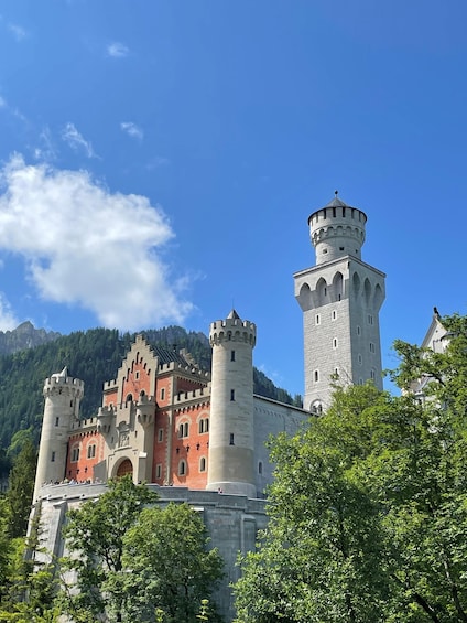 A castle with multiple towers and a red facade, surrounded by lush greenery and mountains. 2