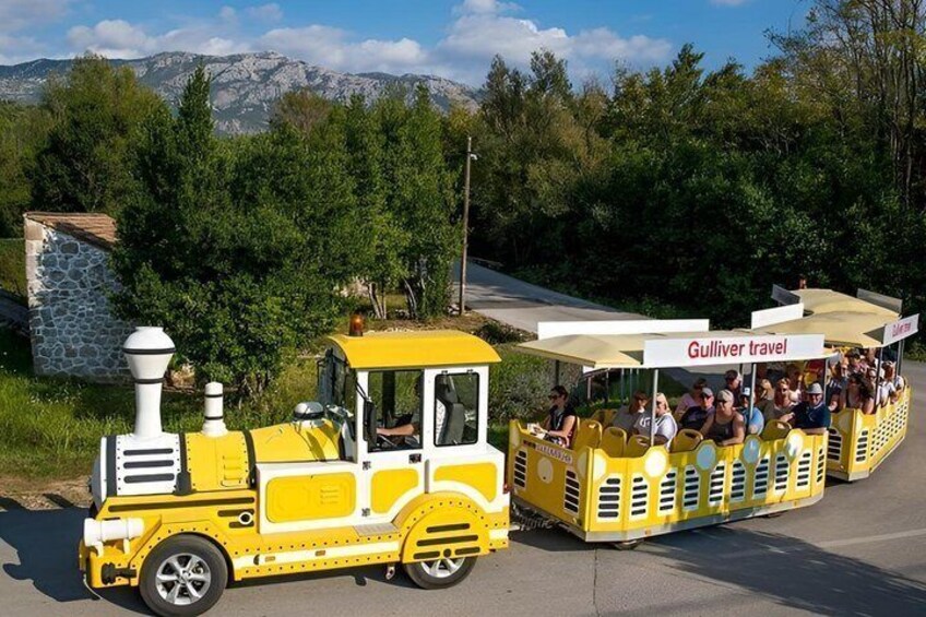 A yellow train with passengers, labeled 'Gulliver travel,' moving along a road with trees and mountains in the background. 2