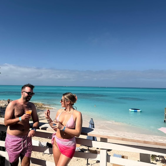 A beach scene with clear turquoise water, a wooden deck, and a person in a pink swimsuit. 1