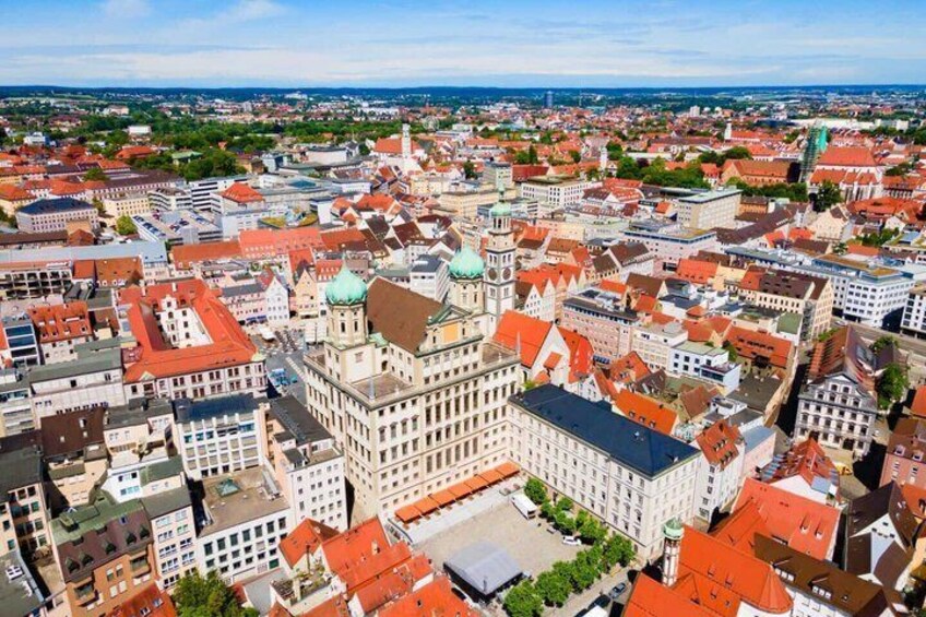 A cityscape with a prominent historical building featuring a green dome and red-tiled roofs. 1