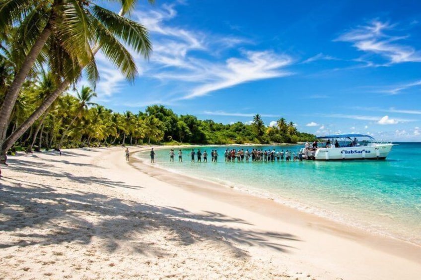 A beach with palm trees, clear turquoise water, and a boat named 'ClubSaras' docked at the shore. 3