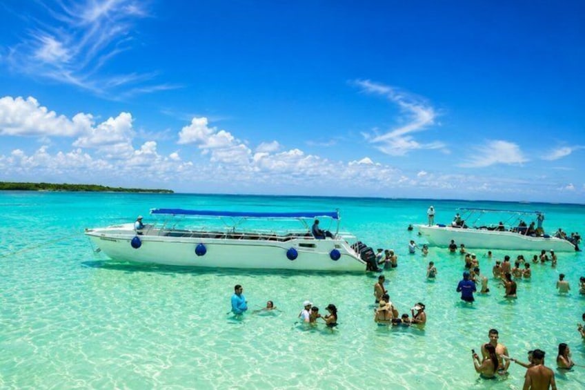 A tropical beach with clear turquoise water, two white boats, and people swimming and enjoying the water. 4