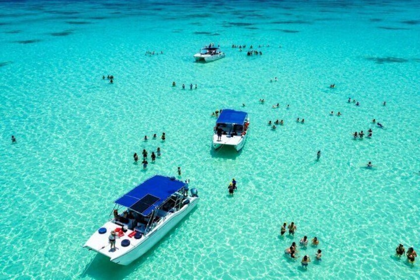 A clear turquoise sea with several boats and people swimming. 5