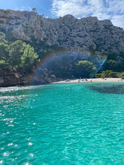 A turquoise sea with people swimming and a rocky mountain in the background. 5