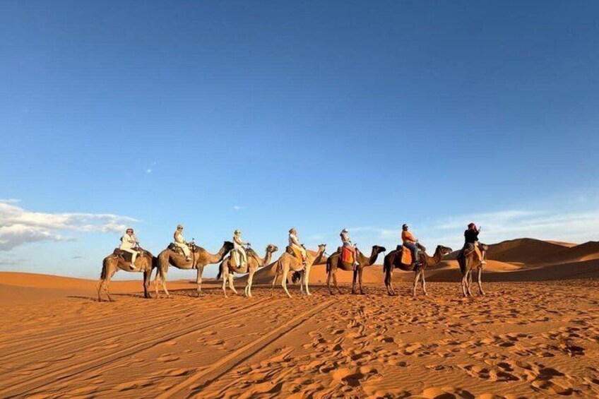 A group of people riding camels across a desert landscape with sand dunes. 1