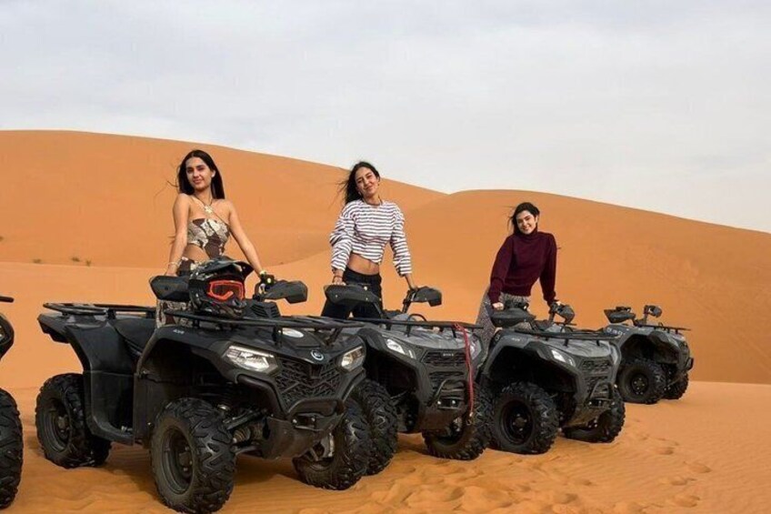 Three ATVs parked on a sandy dune with a desert landscape in the background. 3