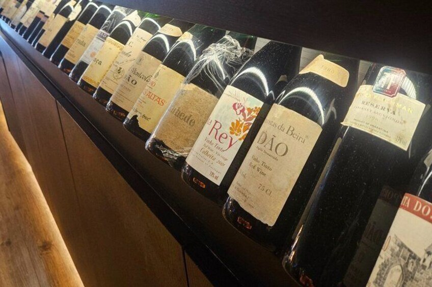 A row of wine bottles with labels, some with corks, on a shelf. 3