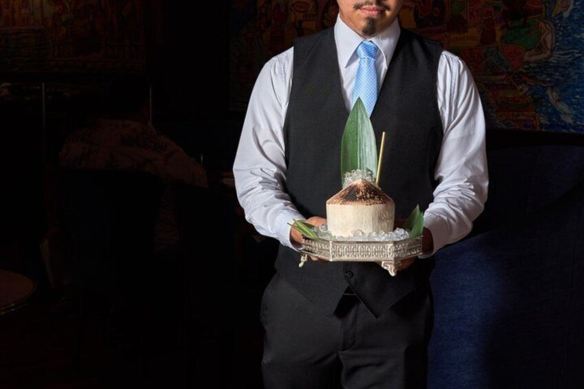 A person in a suit holding a cake with a candle, in a dimly lit room with a couch and a patterned wall. 2