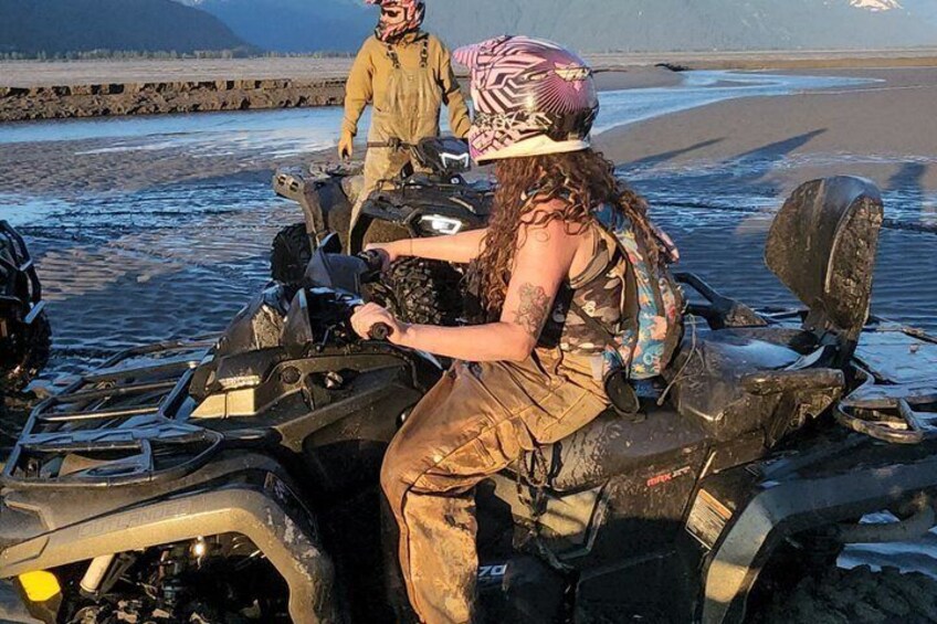 A person on an ATV on a beach with a rocky shoreline and mountains in the background. 3