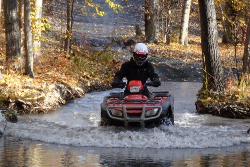 A person riding a red ATV through a forested area with a river. 2
