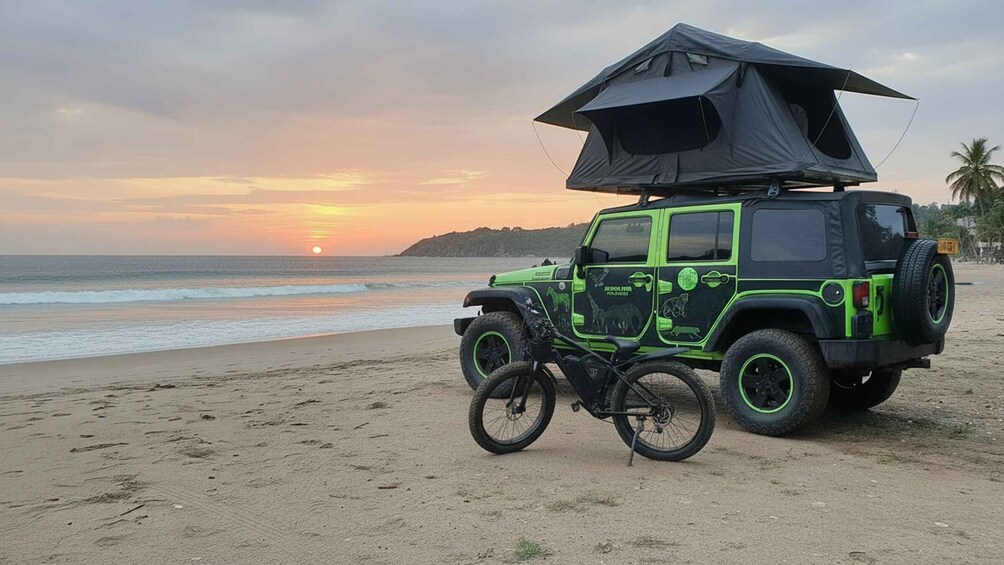 Een groene Jeep met een zwarte tent op een strand bij zonsondergang. 1