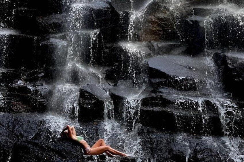 A waterfall cascading over dark rocks with a person lying on the rocks. 5