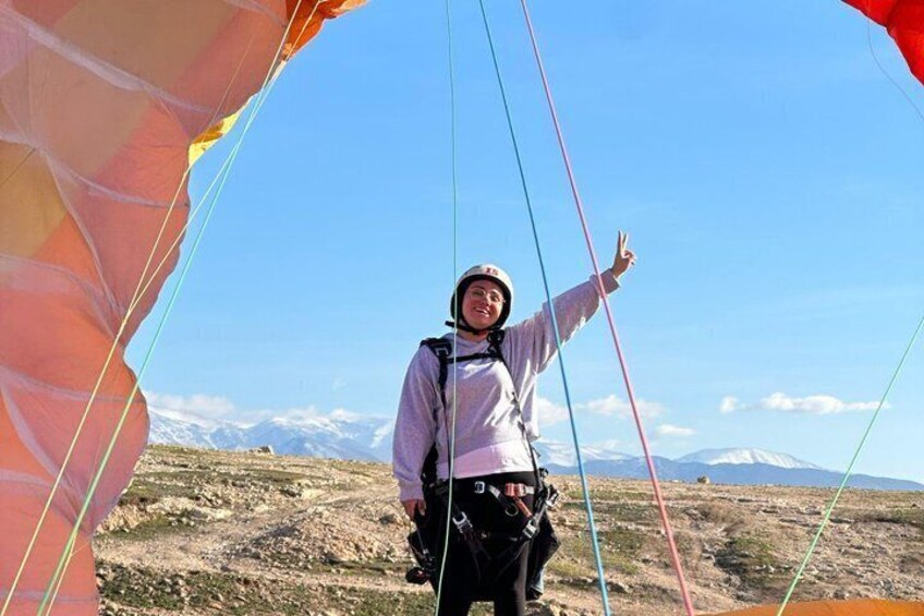 A person with a parachute harness standing on a mountain with a clear sky and snow-capped mountains in the background. 3