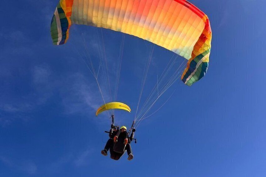 A paraglider with a multicolored canopy against a clear blue sky. 2