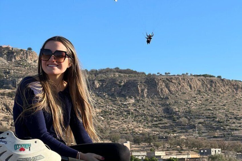 A person with long hair, a white bag, and a mountainous landscape in the background. 4