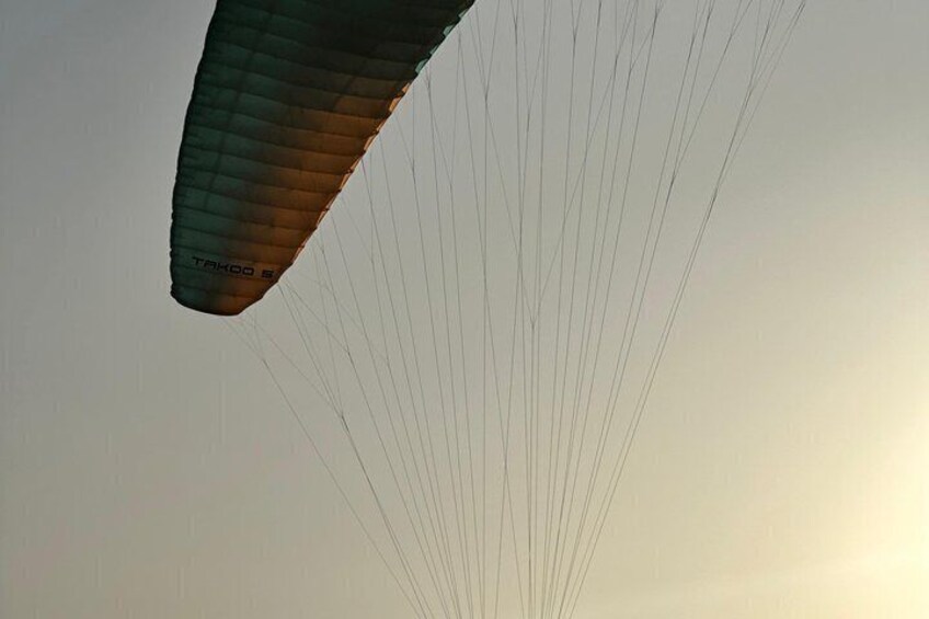 A paraglider with the brand 'TAKOO 5' against a clear sky. 5