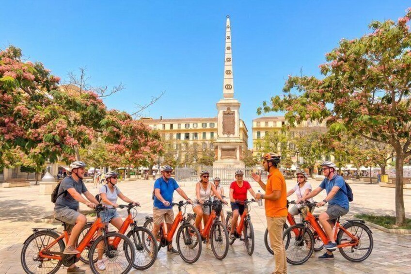 A group of cyclists in a plaza with a tall monument in the background. 3