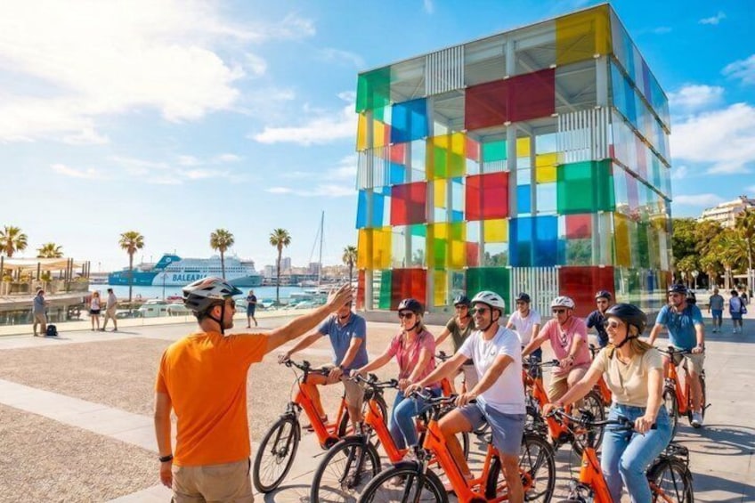 A group of cyclists in front of a colorful modern building. 1