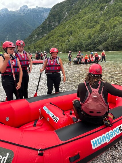 A group of people in a red inflatable raft on a river, surrounded by mountains and greenery. 2