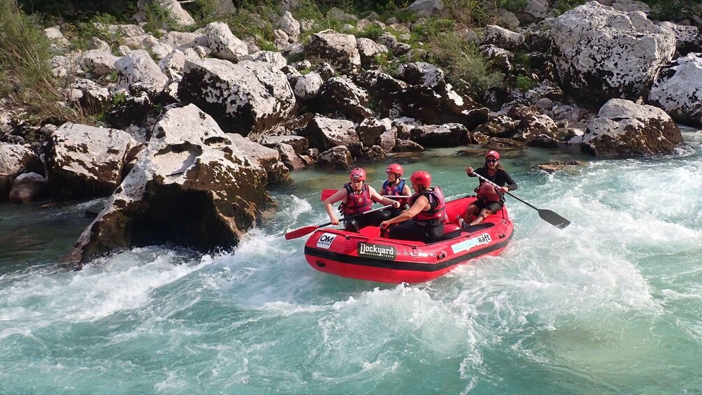 A group of people in a red raft navigating a river with rocky banks. 3
