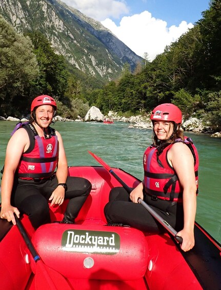 Two people in a red raft on a river with mountains in the background. 4