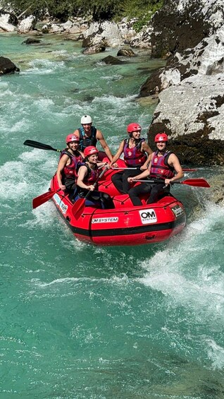 A group of people in a red inflatable raft navigating a river with clear water and rocky banks. 5