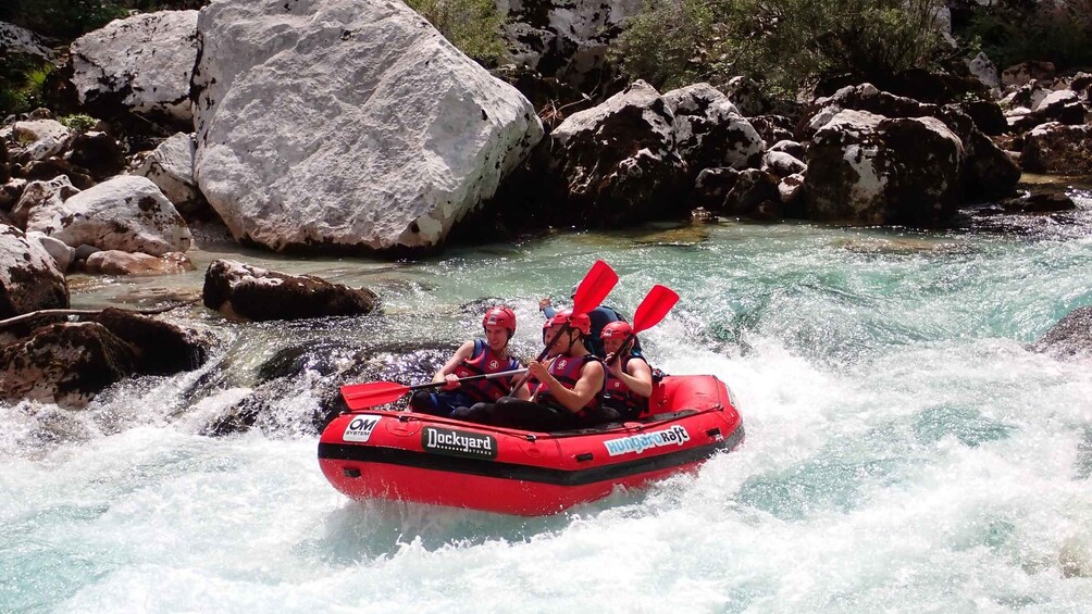 A group of people rafting on a river with white water rapids, surrounded by large rocks and greenery. 5