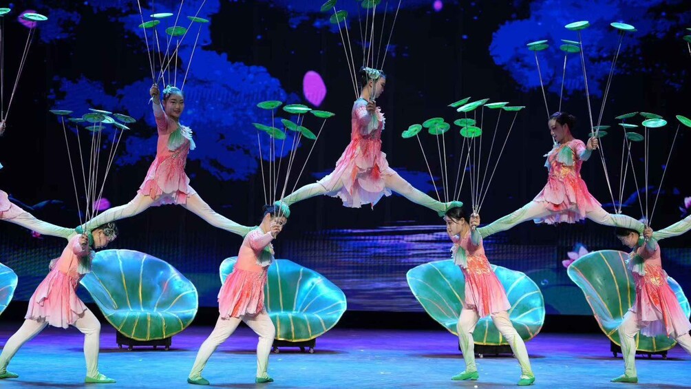 A dance performance with performers in pink costumes and green shoes, with a backdrop of blue and purple lighting. 4