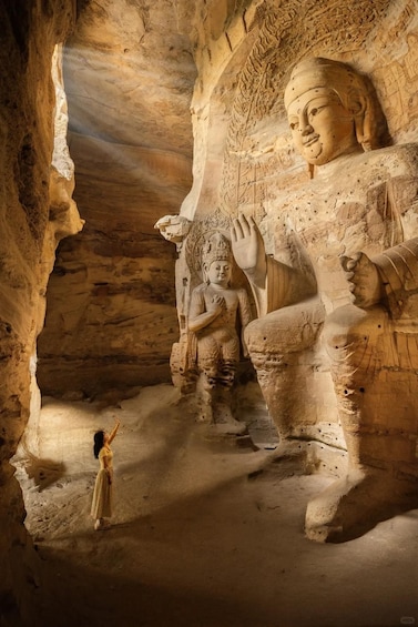 A large Buddha statue in a cave with intricate carvings and a person standing in front of it. 1