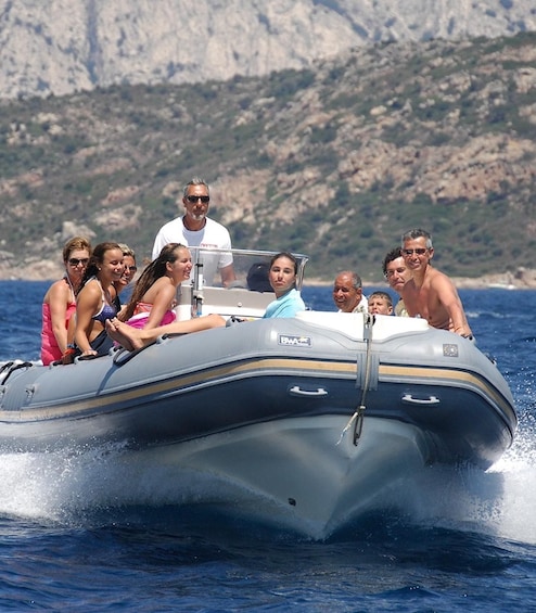 A group of people on a motorboat with a rocky coastline in the background. 1