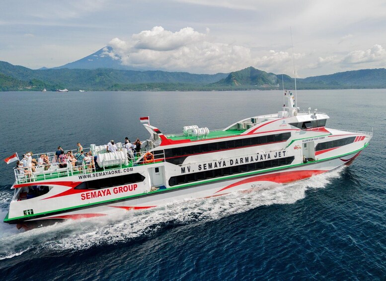 A white and red ferry named MV Semaya Darma Jaya Jet with passengers, sailing on a calm sea with mountains in the background. 1
