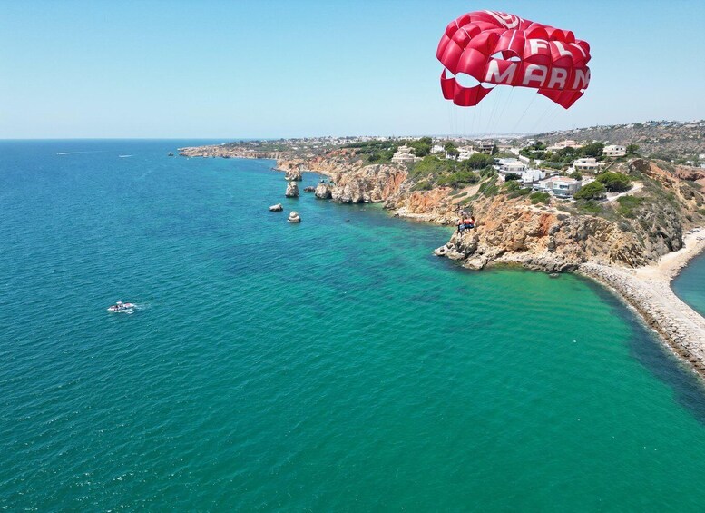 A coastal landscape with clear turquoise waters, a rocky shoreline, and a red parachute with the word 'FLY' visible. 2