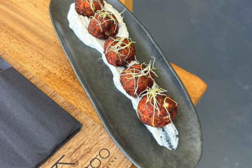 A plate of meatballs with a creamy sauce and garnish, on a dark plate. 4