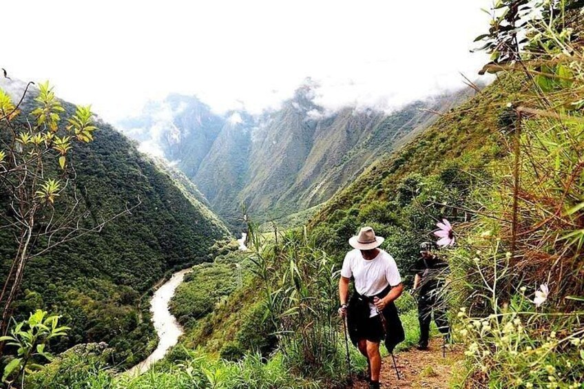 A hiker on a trail with a river in the valley and mountains in the background. 1