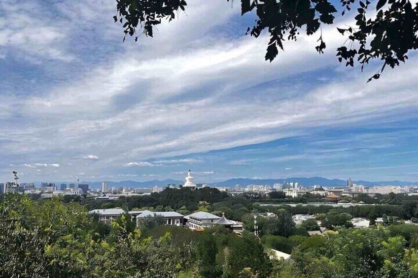 A cityscape with a prominent white pagoda, lush greenery, and distant mountains under a partly cloudy sky. 4