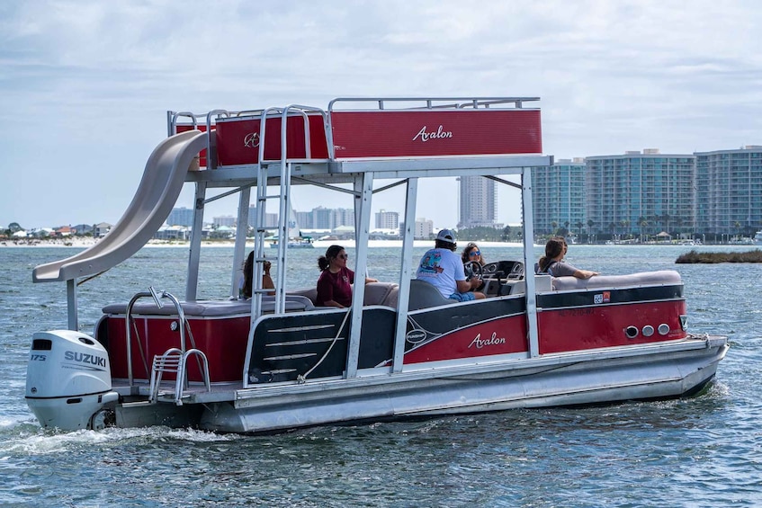 A red and white boat with a slide, labeled 'Avalon,' on water with a city skyline in the background. 3