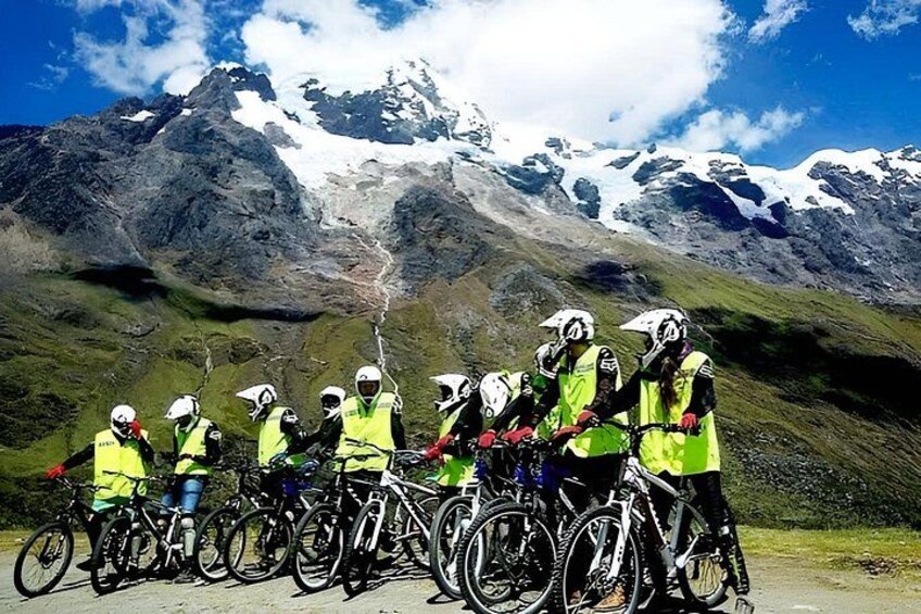 A group of cyclists in reflective vests on a mountain road with snow-capped peaks in the background. 3