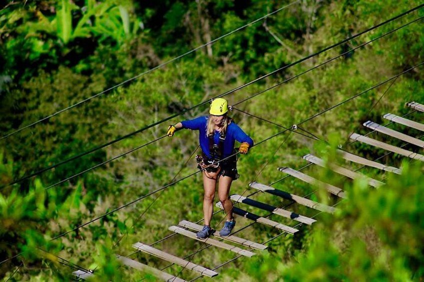 A person on a zip line course with wooden planks and cables. 2